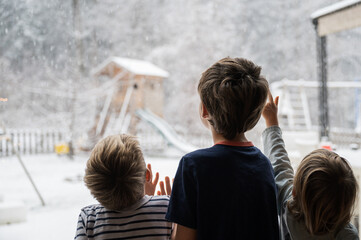 View from behind of three children, siblings, looking out the window into a beautiful winter nature - 532087109