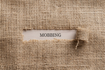 Fototapeta Rough linen fabric with a torn window in the middle with the word MOBBING written in it obraz