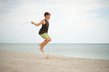 The boy is jumping rope on the beach. Sea and sand. Outdoor sports. Lifestyle.
