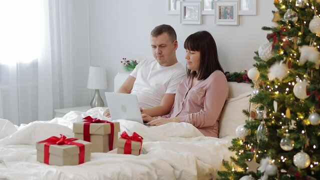 christmas and online shopping concept - happy couple choosing christmas presents online 