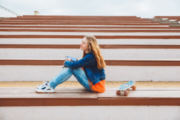 Portrait of a smiling young teenage girl sitting on a park bench and listening to music. Listening to music with headphones .generation z.