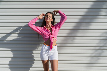 Young beautiful brunette woman in a pink shirt and white denim shorts against the background of a...