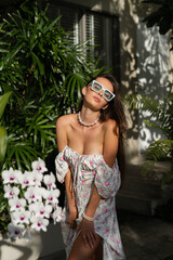 Young beautiful woman in a romantic dress with a floral print, sunglasses and a pearl necklace...