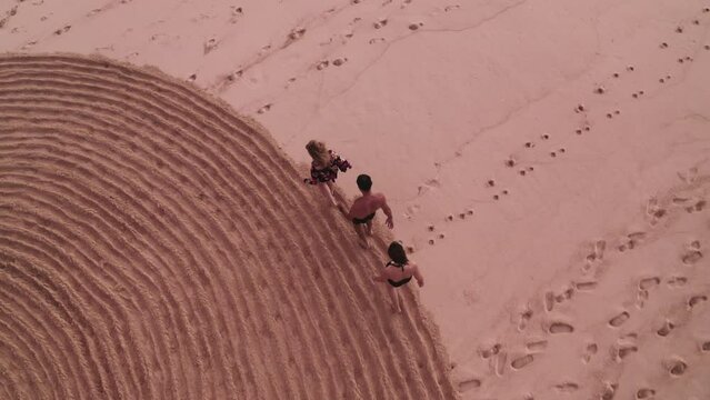 Aerial top view follow people trampling down mysterious spiral circle on sand. Fake mystery and sports exercise for tourists on seaside. Rite with ancient symbol. Enigmatic sign on sandy beach.