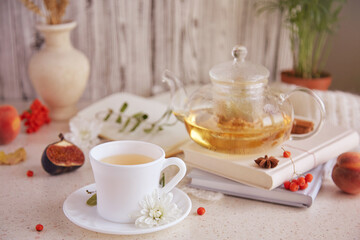 Obraz na płótnie Canvas Natural herbal organic linden tea in teapot and cup of tea. Dry fragrant flowers, autumn arrangements, figs, peaches and book. Cozy atmosperic home.