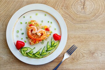 Heart shaped shrimp fried rice served with heart shaped cucumbers and tomatoes on plate with wooden background.Creative art food idea for Valentine or Mother's day.Top view.Copy space