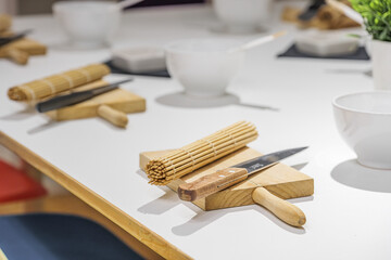 Sets of knife, board and bamboo sushi mat on white table before sushi master class. Education,...
