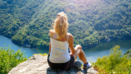 Woman on mountain peak admiring panoramic view (river and mountain with forest)