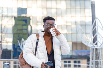 Man using phone with wireless headphones walking in the city and drinking coffee.