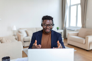 Focused African man wear headphones with microphone looking at laptop screen listens audio lesson...