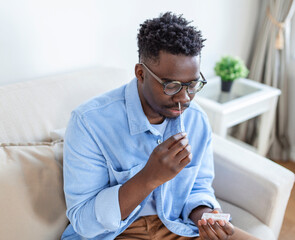 Naklejka premium African-American man using cotton swab while doing coronavirus PCR test at home. man using coronavirus rapid diagnostic test. Young man at home using a nasal swab for COVID-19.