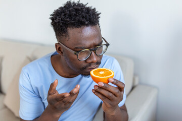 Sick Arican man trying to sense smell of half fresh orange, has symptoms of Covid-19, corona virus infection - loss of smell and taste. One of the main signs of the disease.