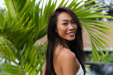 Beautiful asian thai woman with soft smooth clean dark tanned skin posing outdoor  in white dress with tropical background