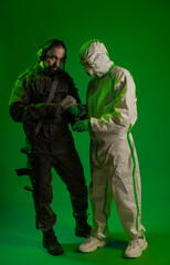 a soldier in a studio on a green background with a medic or scientist in a white protective suit. a man in military uniform rifle or machine gun carries a person in chemical protection on his shoulder