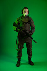 a soldier in the studio on a green background puts on a white mask on his face. man in military uniform with a rifle or machine gun