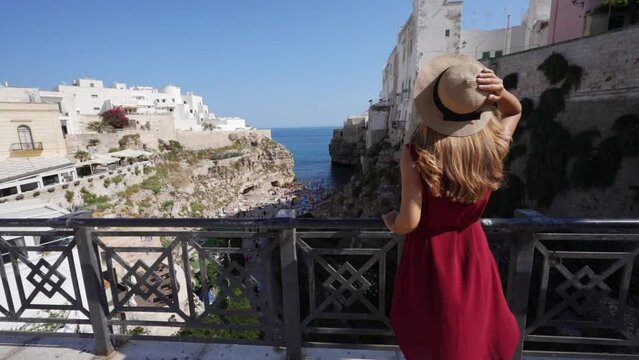 Traveling in Italy. Young tourist girl enjoying view of Lama Monachile in Polignano a mare, Apulia, Italy. Slow motion.