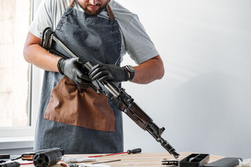 Close up of young man in apron disassembling a gun above the table