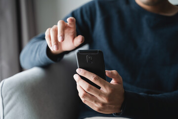 Happy man using smart phone touching virtual screen on sofa in living room at home, searching data and social media on internet.