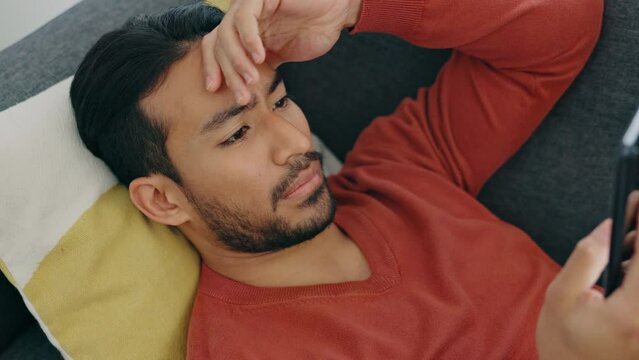 Stress, shock and man texting on phone, shocked by bad news, scam alert or a breakup text. Confused, unhappy and worry with young male surprised by app message, feeling puzzled and nervous in home