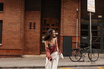 Positive young caucasian woman spends her weekends walking around city during day. Brunette in good...
