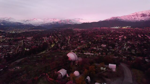 Aerial dolly in view of the Cerro Calan observatory with the snow-capped Andes Mountains in the background of Santiago, Chile. Purple sunset