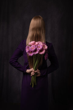 Abstract studio portrait of blonde woman with pink gerbera flowers seen from back