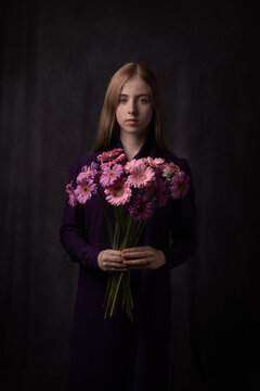 Classic dark studio portrait of young woman with pink gerbera flowers