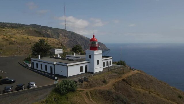 Aerial view of the Ponta do Pargo light house in the south coast of Madeira island. Drone rotating to the right showing the light house and some tourists in the background. 4K, 60fps.