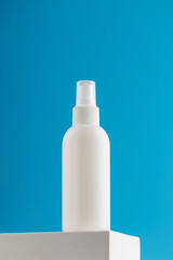 White spray mockup with air freshener or cosmetic product on a pedestal on a blue background with a delicate flower.