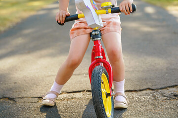 Closeup of legs of little girl running with balance bike on summer day. Happy child driving, biking...
