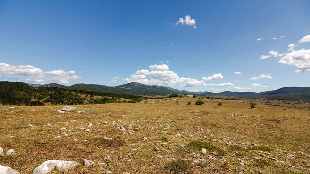 Time lapse shot of a stony grass steppe near Komic with some bushes and trees at sunny noon with some clouds