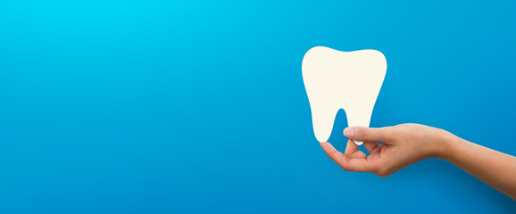 Woman hand holding tooth shape at blue background,  dental care concept.