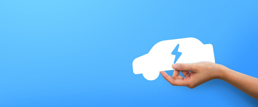 Woman hand holding car electrics shape at blue background,  clean energy concept.