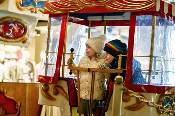 Little preschool girl and school boy riding on ferris wheel carousel horse at Christmas funfair or market, outdoors. Two happy children having fun on traditional family xmas market in Germany