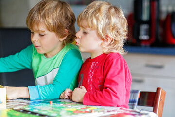 Two little blond kid boys playing together board game at home. Funny siblings having fun. Twins and...