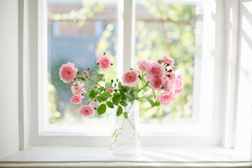 Fototapeta na wymiar Bouquet of summer roses in glass vase near the window