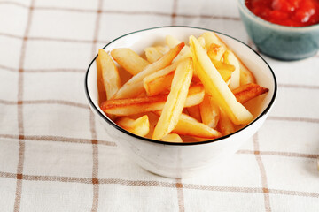 French fries in awhite bowl on light checkered background. 