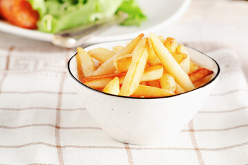 French fries in awhite bowl on light checkered background. 