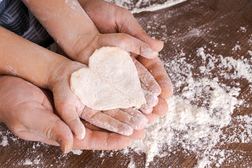 Top view father and child's hand, cut out heart shaped cookies from dough on hands on the background of a wooden table with loose flour. Flat failure.