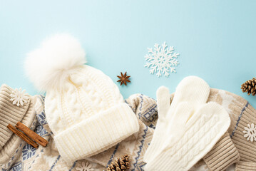 Top view photo of white knitted mittens bobble hat warm sweater snowflakes pine cones anise and cinnamon sticks on isolated light blue background