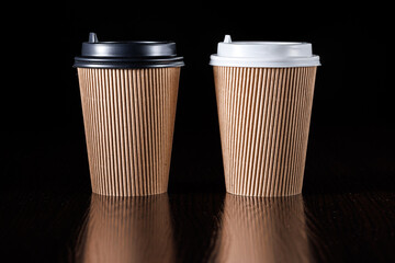 Brown paper cup for hot coffee, tea, drinks with black and white lids on a black background. Side view.
