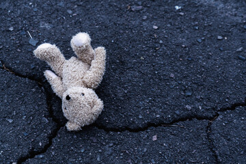 Conceptual image: Teddy bear lies on the street as symbol of children's loneliness, pain, broken childhood and loss future. Copyspace for text or design.