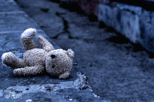 Teddy bear toy forgotten on the street as symbol of children's loneliness, pain, broken childhood and loss future. Copy space.