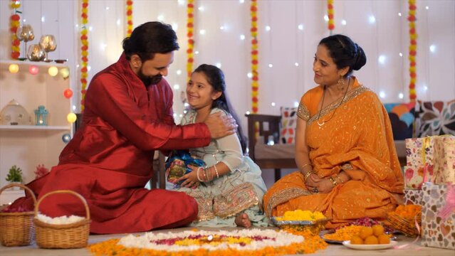 Diwali celebration with gift box exchange - Indian man with his wife and little daughter - Diwali gift  festive background. A happy Indian couple sitting on the floor - Floral rangoli  Diwali rango...