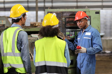 Technician engineer in protective uniform with hardhat standing and teaching apprentices or colleague worker to use computerized machine control at heavy industry manufacturing factory