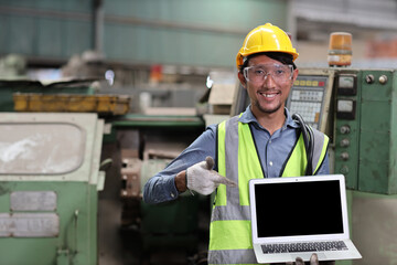 Technician engineer or worker in protective uniform standing and showing blank screen computer while controlling operation or checking industry machine process at heavy industry manufacturing factory