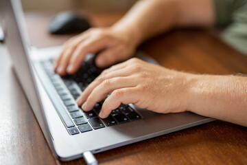 Close-up photo of male hands with laptop. Man is working remotely at home. Distance job