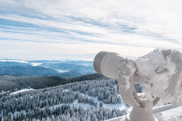 Tourist panoramic telescope overlooking of winter coniferous forest valley in Rhodope Mountains from observation deck on Snezhanka TV tower in ski resort of Pamporovo, Bulgaria