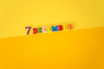 December 7 on yellow and paper background with wooden and multicolored letters with space for text.