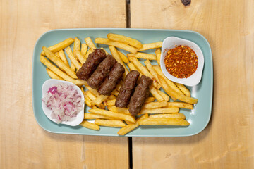 Kebabs served on a wooden board with french fries and onion